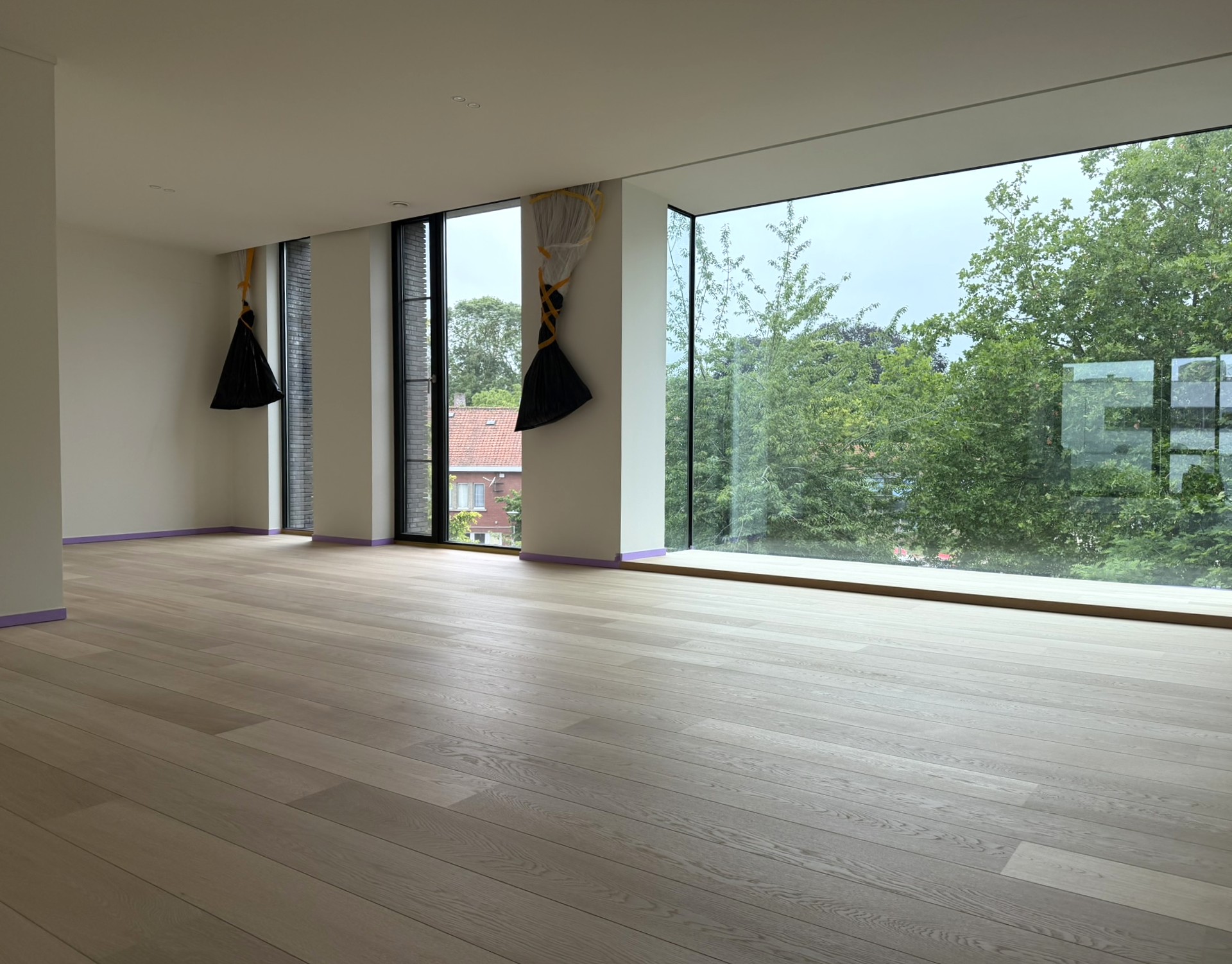 Ruime lichte eiken plankenvloer in een woning met grote raampartij en zicht op groen